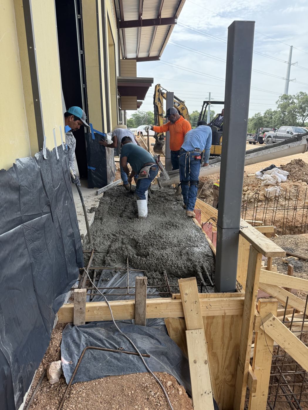 Crew pouring concrete along the building, Avenue N commercial site work